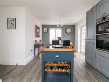 A kitchen with a blue island and wine rack and dining table with chairs at Beacon House in St Agnes