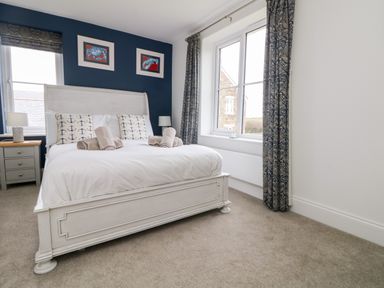 A bedroom with a white bed with anchor pillows and rolled towels bedside tables and patterned curtains at Beacon House in St Agnes