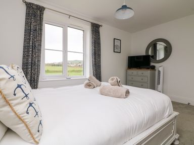 A bedroom with a white bed and rolled towels a chest of drawers with a TV and a round mirror at Beacon House in St Agnes