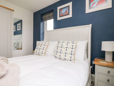 A bedroom with a white bed with anchor patterned pillows next to a nightstand with a lamp at Beacon House in St Agnes
