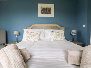 A bed with white linens and patterned pillows against a blue wall with lamps on bedside tables at Beacon House in St Agnes