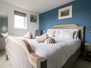 A bedroom with a double bed with white bedding and towels on top next to a window and a nightstand with a lamp at Beacon House in St Agnes