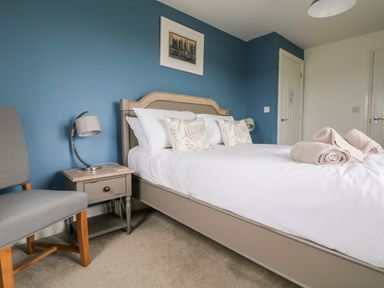 A bedroom with a bed with rolled towels and cushions a bedside table with a lamp and a chair at Beacon House in St Agnes