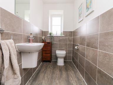 A bathroom with a wall-mounted sink a towel hanging a toilet a wooden cabinet and wall art at Beacon House in St Agnes