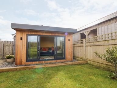 A wooden garden room with glass sliding doors and a sofa inside at Beacon House in St Agnes