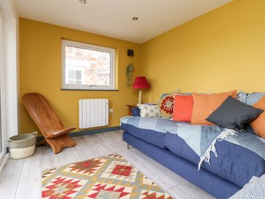 A sitting room with a blue sofa and colorful cushions a wooden chair and a patterned rug at Beacon House in St Agnes