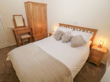 A bedroom with a double bed three pillows on the bed two bedside tables with lamps a wardrobe and a dressing table with a stool at Tyddyn Sianel - Derw in Llanystumdwy near Criccieth