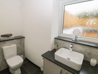A bathroom with a toilet towels a rectangular sink and a textured glass window at Tyddyn Sianel - Derw Llanystumdwy near Criccieth