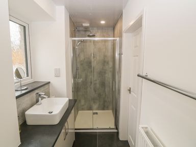 A bathroom with a shower enclosure a sink countertop and a window at Tyddyn Sianel - Derw Llanystumdwy near Criccieth
