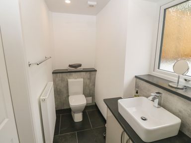 A bathroom with a toilet a sink on a countertop a window and a towel rack at Tyddyn Sianel - Derw in Llanystumdwy near Criccieth