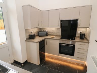 A kitchen with grey cabinets black appliances and under cabinet lighting at Tyddyn Sianel - Derw in Llanystumdwy near Criccieth