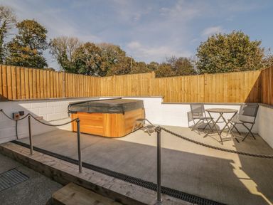 An outdoor patio area with a hot tub and a small table with two chairs surrounded by wooden fencing at Tyddyn Sianel - Derw in Llanystumdwy near Criccieth