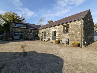 Stone buildings with benches and flower pots in a courtyard at Tyddyn Sianel - Derw in Llanystumdwy near Criccieth