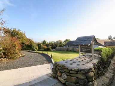 An entrance area with a stone wall and sign for Tyddyn Sianel Holiday Lets and gravel driveway at Tyddyn Sianel - Derw Llanystumdwy near Criccieth