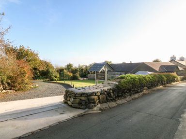 A driveway and stone wall with a sign for Tyddyn Sianel Holiday Lets near houses and trees at Tyddyn Sianel - Derw in Llanystumdwy near Criccieth