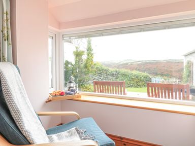 A chair with a blanket next to a window showing outdoor chairs and a garden at Glenhaven in Trewarmett near Tintagel