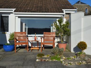 A patio with two wooden chairs and a small table with a wine bottle and glasses at Glenhaven in Trewarmett near Tintagel