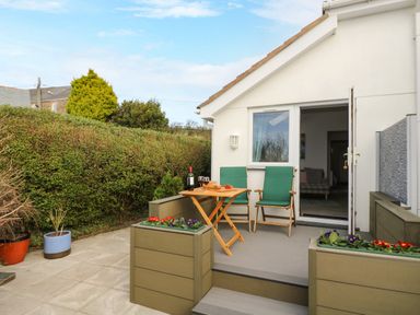A patio with two green chairs and a wooden table with wine glasses outside a white house at Glenhaven in Trewarmett near Tintagel