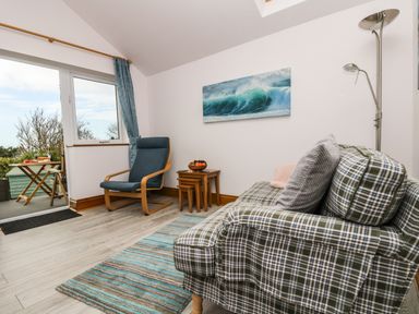 A sitting room with a patterned sofa a blue armchair a wooden side table and a floor lamp at Glenhaven in Trewarmett near Tintagel