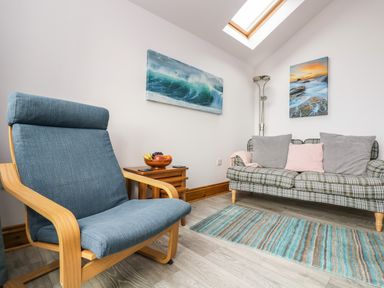 A living room with a blue armchair a plaid sofa with cushions a striped rug and seascape paintings at Glenhaven in Trewarmett near Tintagel