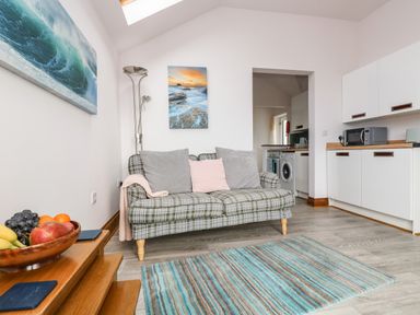 A living room with a plaid sofa and cushions next to a kitchen area at Glenhaven in Trewarmett near Tintagel