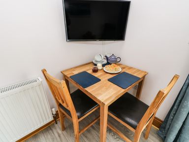 A small wooden dining table with two chairs a teapot scones and jam and cream below a wall mounted television at Glenhaven in Trewarmett near Tintagel