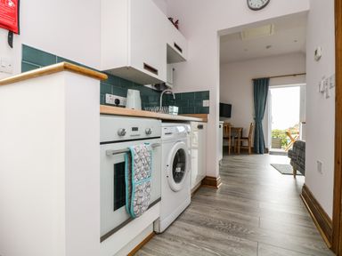 A kitchen with an oven a washing machine a countertop and cabinets next to a living area with a table chairs and a door at Glenhaven in Trewarmett near Tintagel