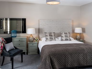 A bedroom with a bed with grey quilt and patterned pillows two bedside tables with lamps a chair and a dresser at Oakdene Country House in Sedbergh