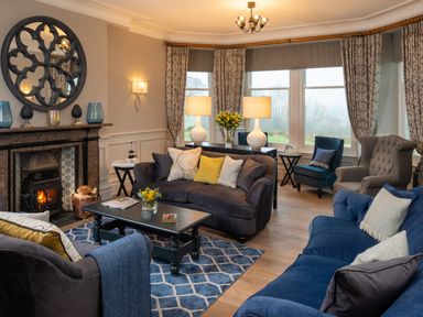 A living room with sofas armchairs a coffee table a fireplace and large windows with curtains at Oakdene Country House in Sedbergh