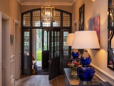 An entryway with stained glass doors a console table with blue lamps and flowers at Oakdene Country House Sedbergh