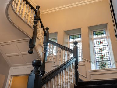 A staircase with dark wood handrails and white balusters near stained glass windows at Oakdene Country House in Sedbergh