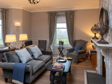 A living room with a sofa, two armchairs, coffee table, window with curtains and a fireplace at Oakdene Country House Sedbergh