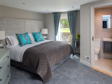 A bedroom with a large bed and blue pillows next to a window with blue curtains and an adjoining bathroom at Oakdene Country House in Sedbergh