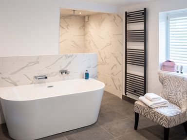 A bathroom with a white bathtub a patterned chair with towels and a black towel rack at Oakdene Country House in Sedbergh