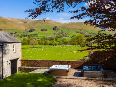 A garden with two hot tubs next to a stone house and a field with sheep at Oakdene Country House in Sedbergh