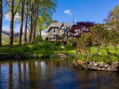 A stone house with a pond lawn chairs and trees at Oakdene Country House Sedbergh
