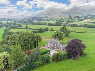 A countryside house surrounded by trees and green fields with hills in the background at Oakdene Country House in Sedbergh