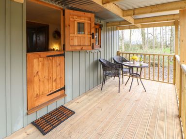 A wooden porch with two wicker chairs and a round table with a bottle and flowers at Bracken Fern in Eppleby