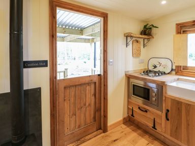 A kitchen corner with wooden cabinets a microwave a gas stove a window and a wooden door at Bracken Fern in Eppleby