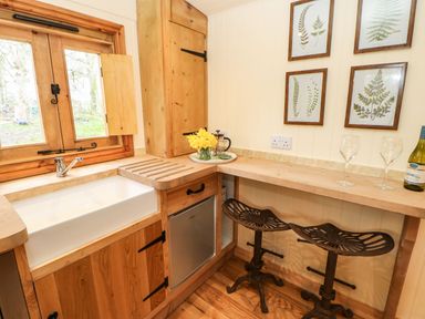 A kitchen corner with a white sink wooden cabinets metal stools and framed botanical prints at Bracken Fern in Eppleby