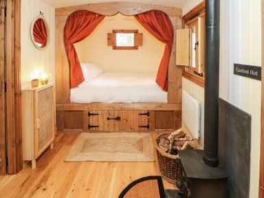 A bedroom with a built-in wooden bed with orange curtains a wood stove with wood basket and a small cabinet with lamp at Bracken Fern in Eppleby