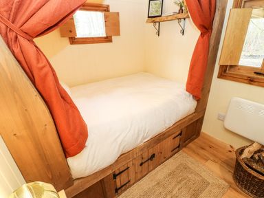 A small bedroom with a wooden framed bed with white bedding and orange curtains at Bracken Fern in Eppleby