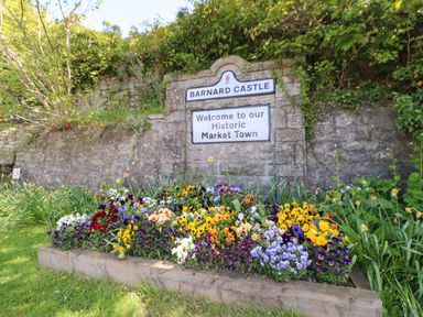 A stone welcome sign for Barnard Castle with flowers planted in front and greenery behind at Bracken Fern in Eppleby