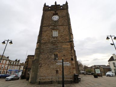 A stone clock tower with benches and signposts in a paved square with surrounding buildings and street lamps at Bracken Fern in Eppleby