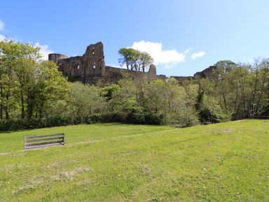An open grassy area with a bench and trees in front of a stone castle ruin under a blue sky at Bracken Fern in Eppleby