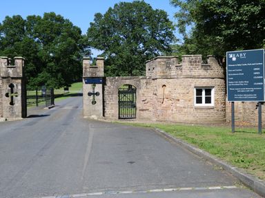 The entrance gate made of stone with a road leading into the park and trees in the background at Raby Castle in Eppleby