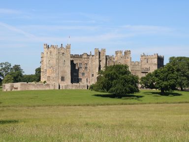 A large stone castle with multiple towers surrounded by green grass and trees at Bracken Fern in Eppleby