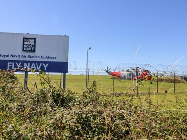 A fenced grassy area with a rescue helicopter and a Royal Navy Air Station Culdrose sign in Helston