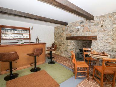 A room with a bar and three bar stools stone walls a fireplace and a round table with four wooden chairs and a chess set at Culdrose Manor in Helston