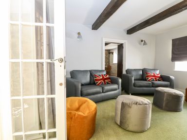 A sitting room with two black leather sofas with union jack cushions and three round poufs at Culdrose Manor in Helston